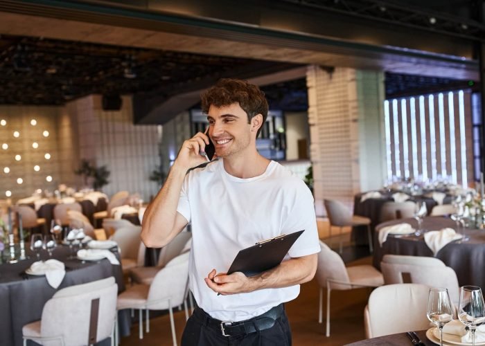 smiling-event-organizer-with-clipboard-talking-on-smartphone-near-festive-tables-in-banquet-hall.jpg